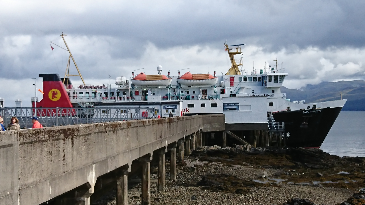 A large ferry docked at a pier with hills in the background.