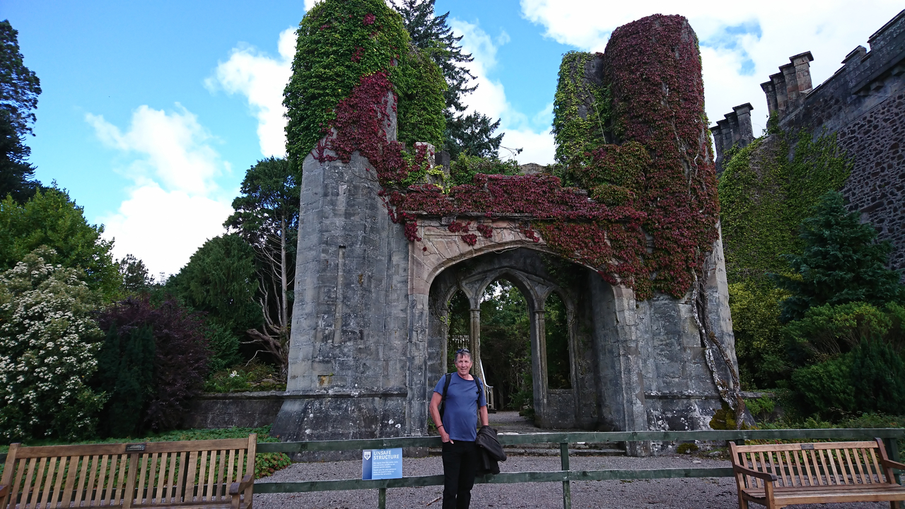 A man standing by a historic stone archway covered in ivy.