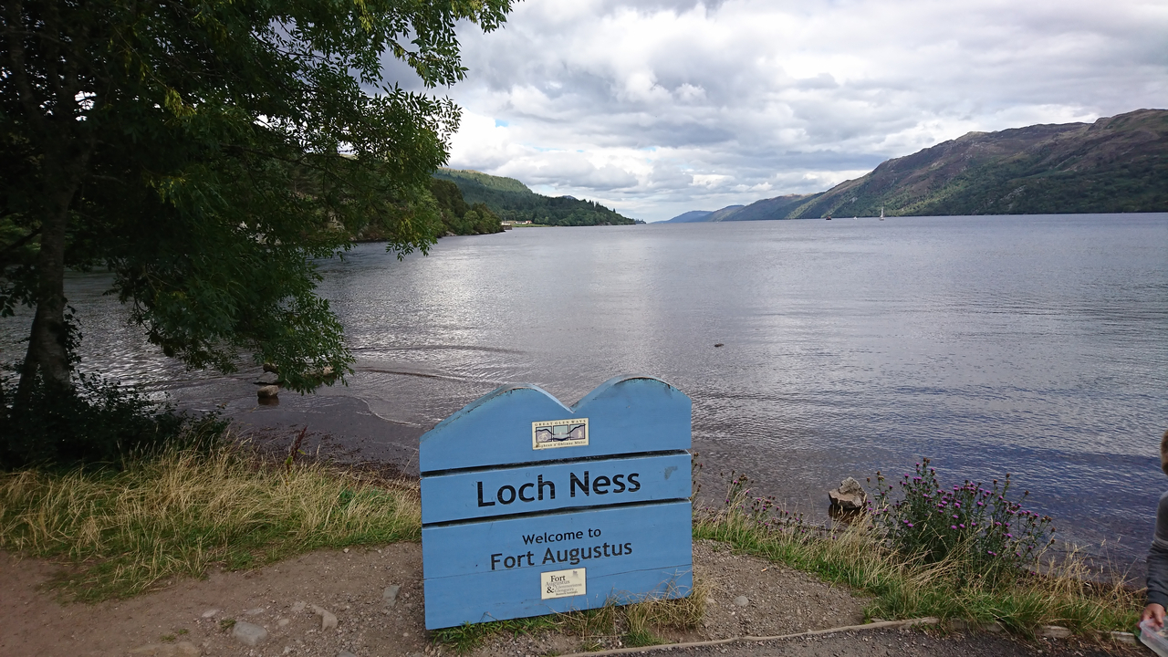 Loch Ness sign near a lake with hills in the background.
