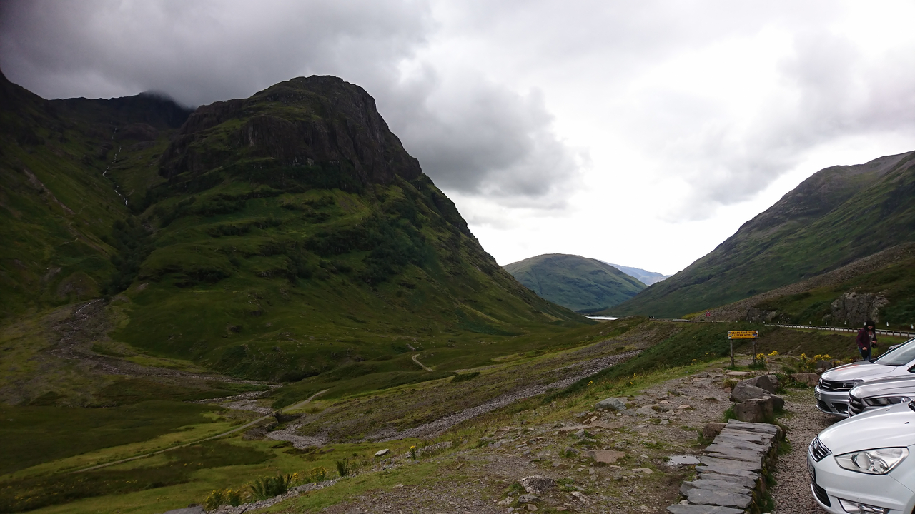 Mountainous landscape with parked cars and moody clouds.