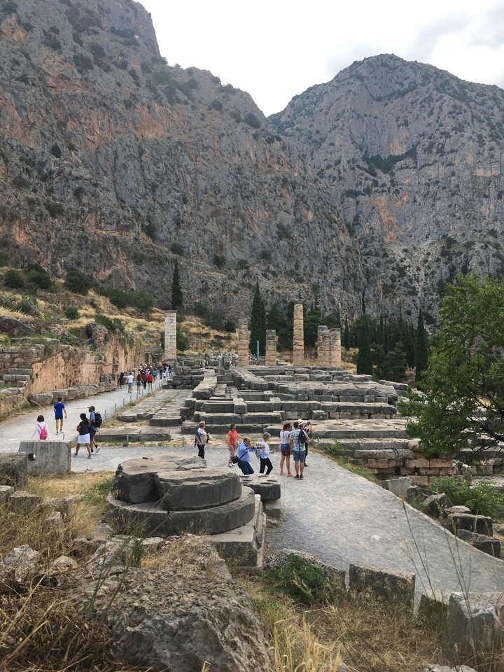 Des touristes se promenant parmi des ruines antiques avec un décor montagneux en arrière-plan.