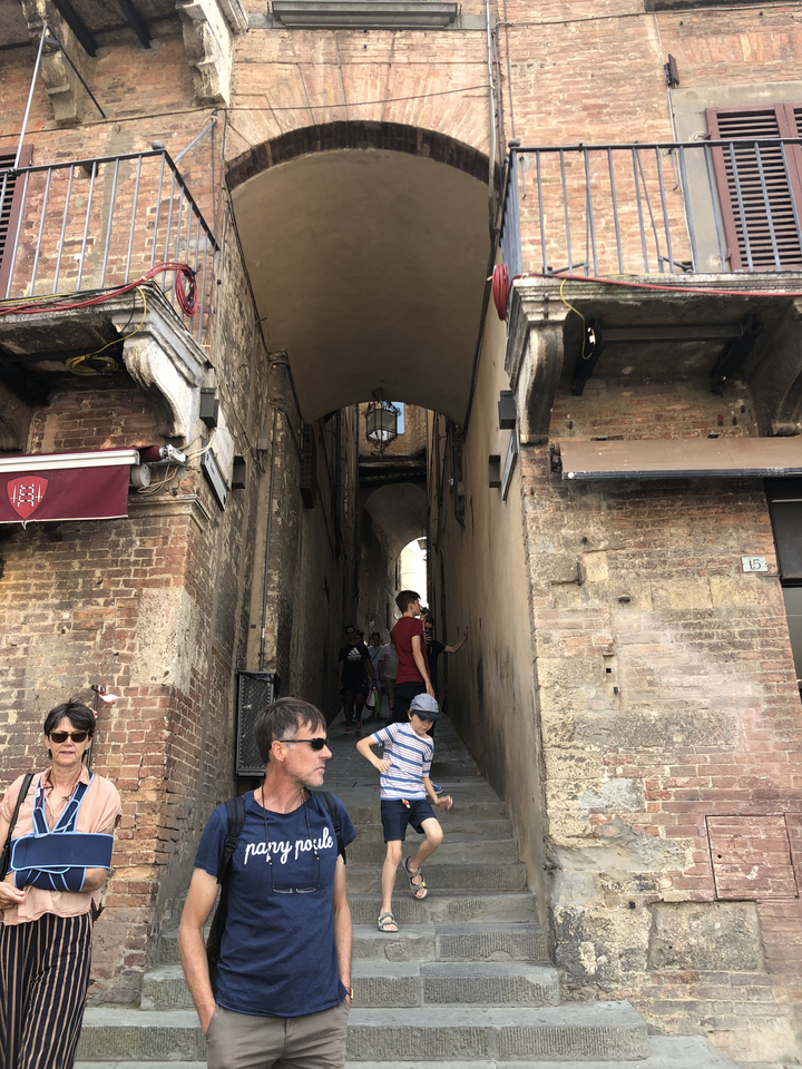 A narrow alleyway with people walking through, surrounded by old brick buildings.
