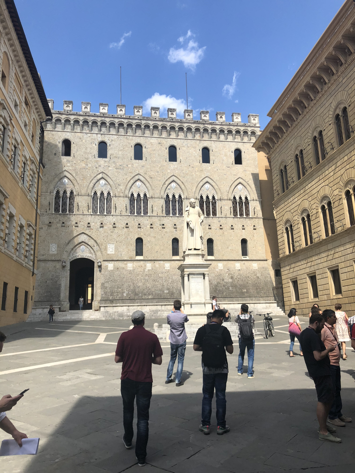 A historic square with a statue and people visiting.