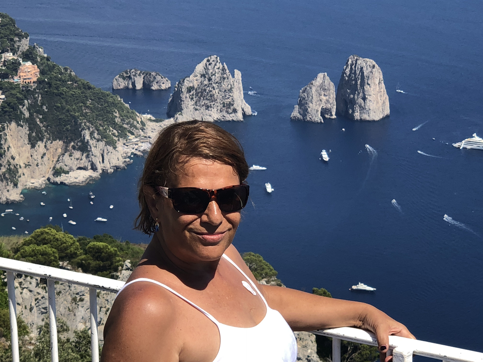 A person with sunglasses posing against a backdrop of rock formations over the sea.