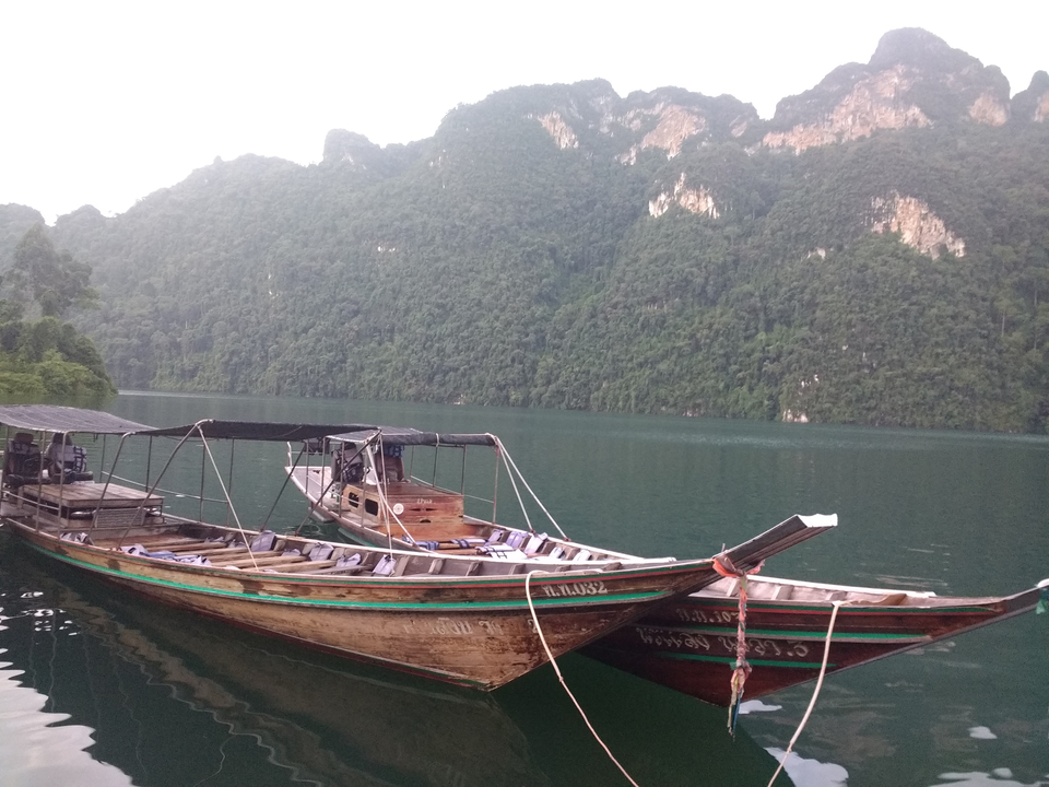Traditional wooden boats on a green lake with forested hills.