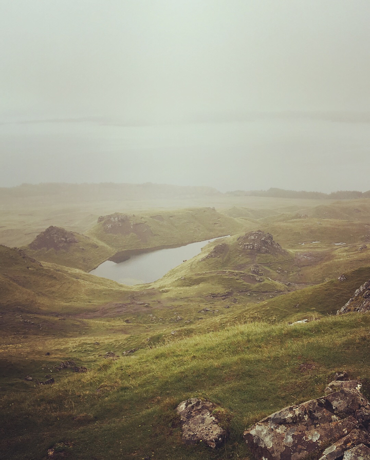 Rolling hills with a small lake under a cloudy sky.