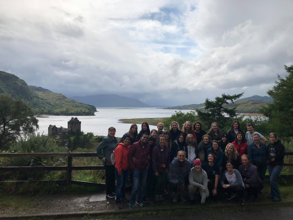 Large group of people posing with a scenic background of water and hills.