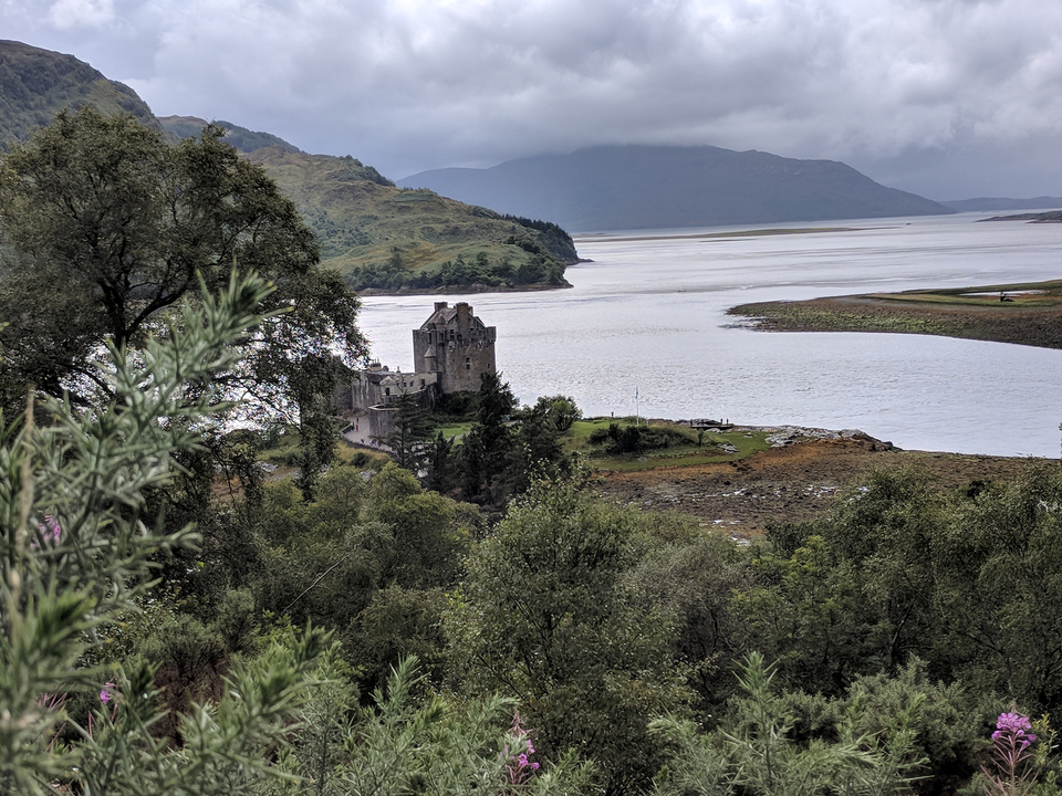 Historic castle by a loch surrounded by lush greenery.