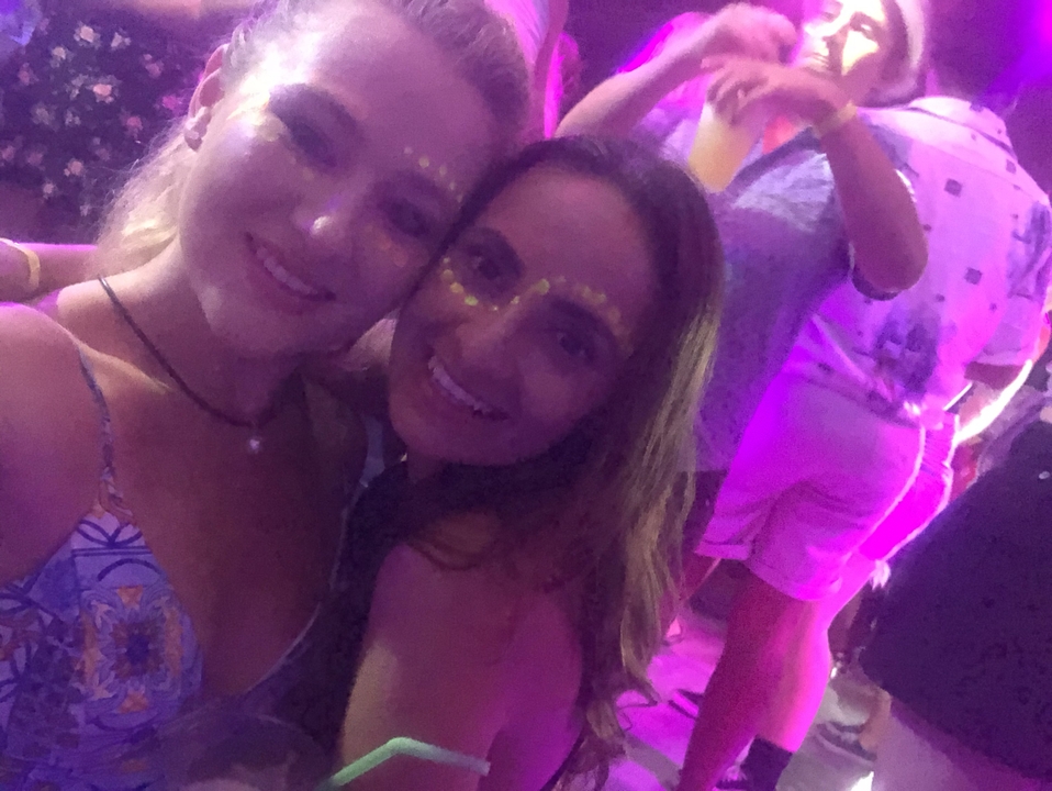 Two women posing together at a party with colorful lighting.