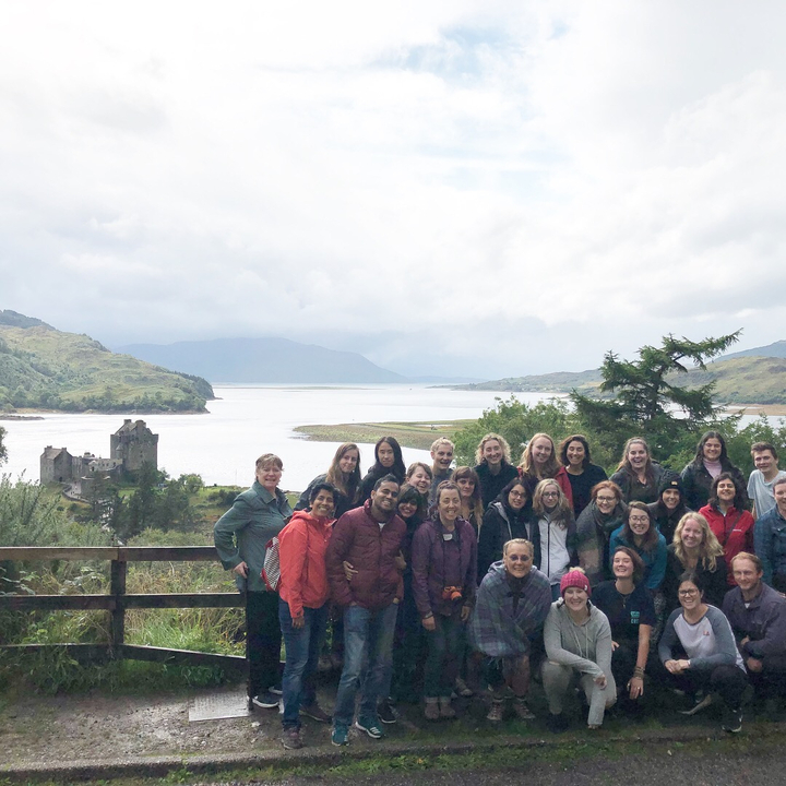 Large group posing with an ancient ruin and lake in the background.