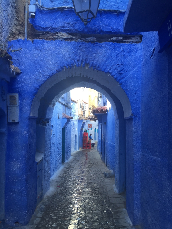 Blue-walled street in Chefchaouen with people walking.