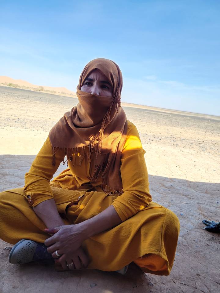 Person in long dress sitting on sand in a desert.