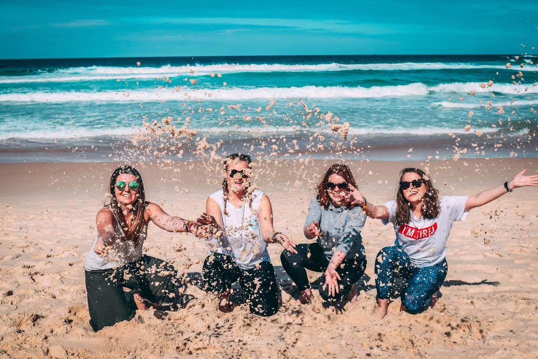 Four women playing with sand at the beach.