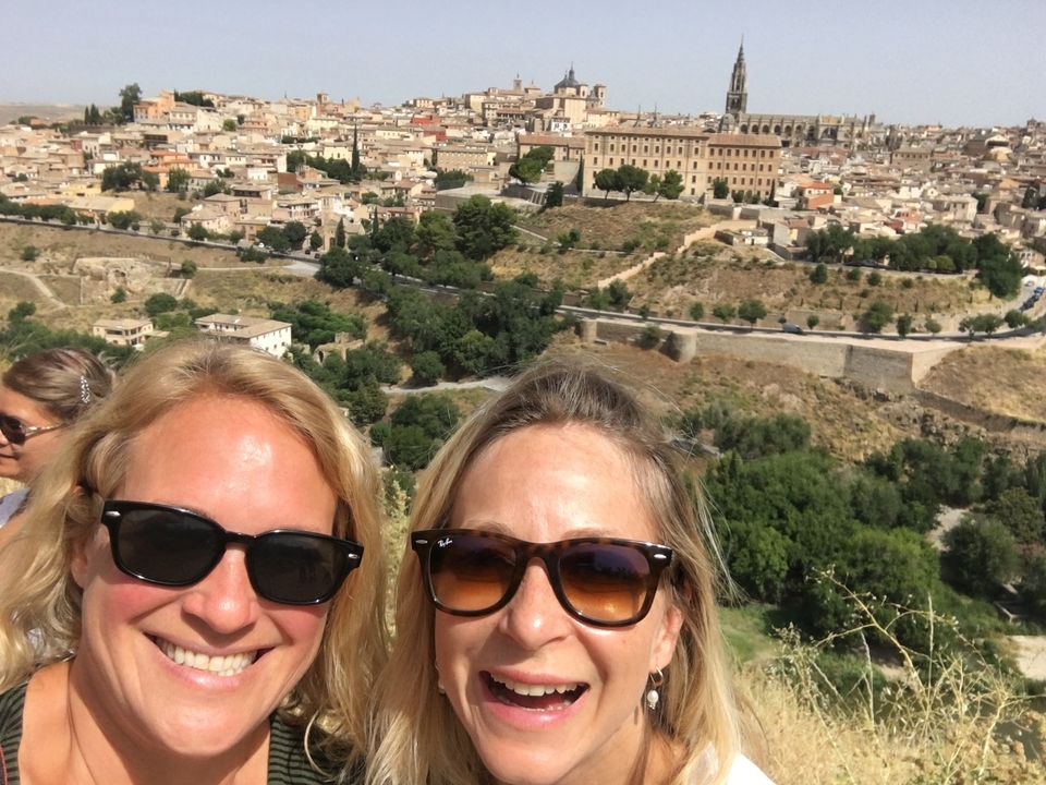 Two women taking a selfie with a scenic town view.
