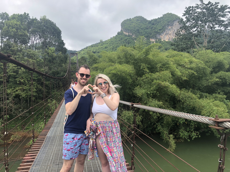 Couple posing on a suspension bridge in a jungle setting.