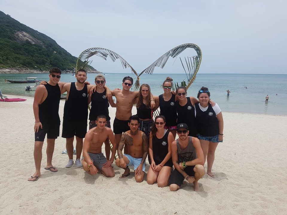 Group of people on a beach posing in front of a heart sculpture.
