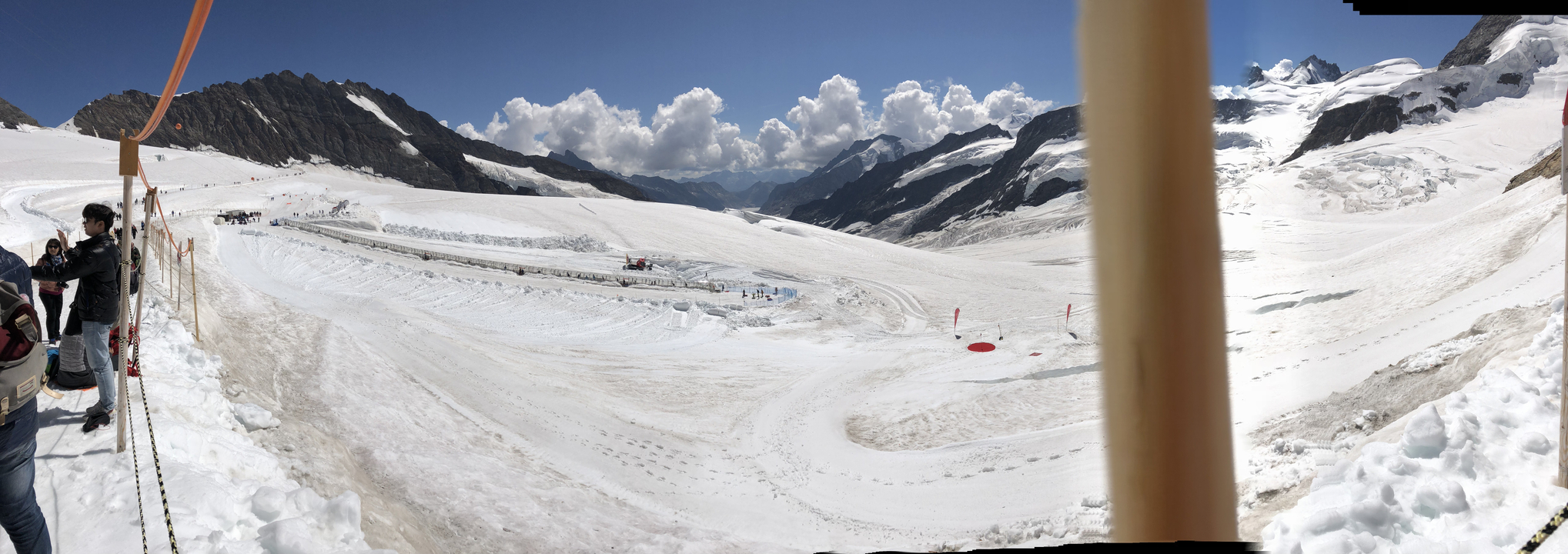 Paysage enneigé avec des montagnes, un poteau en bois et quelques personnes au loin.