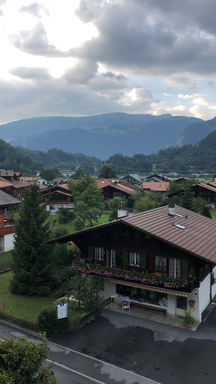 Village alpin avec des maisons en bois et des arbres entourés de montagnes.