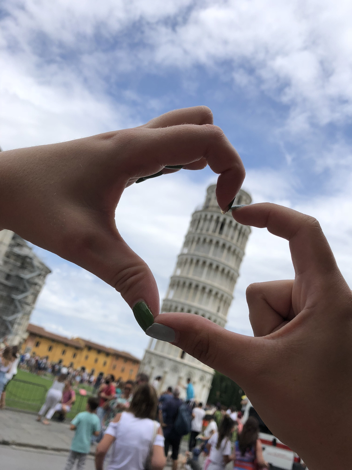 Vue inclinée de la tour penchée de Pise encadrée entre des mains formant un cœur.