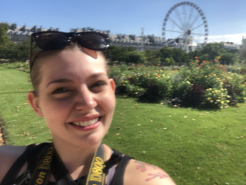 Portrait en gros plan d'une personne à l'extérieur avec une grande roue et des jardins.