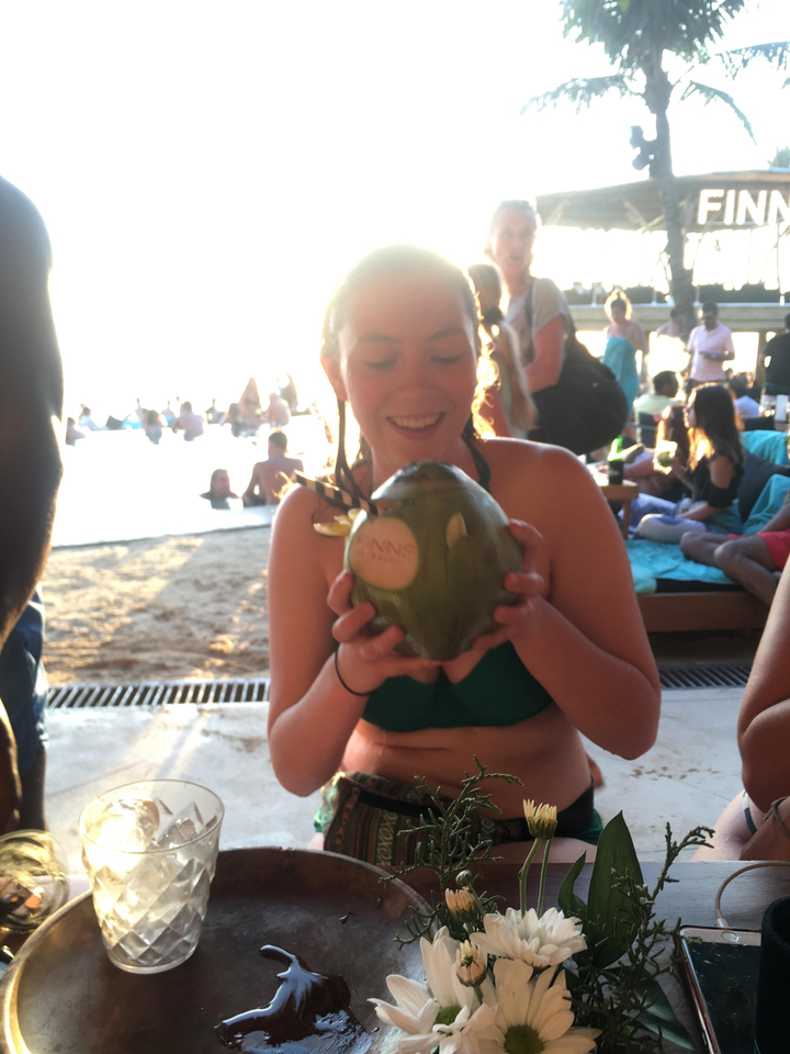 Person holding a coconut by a pool with many people around.