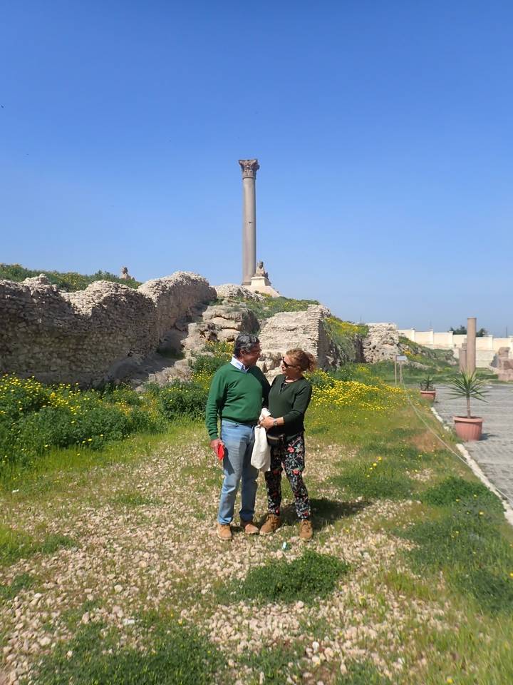 Tourists near an ancient column and grassy ruins.