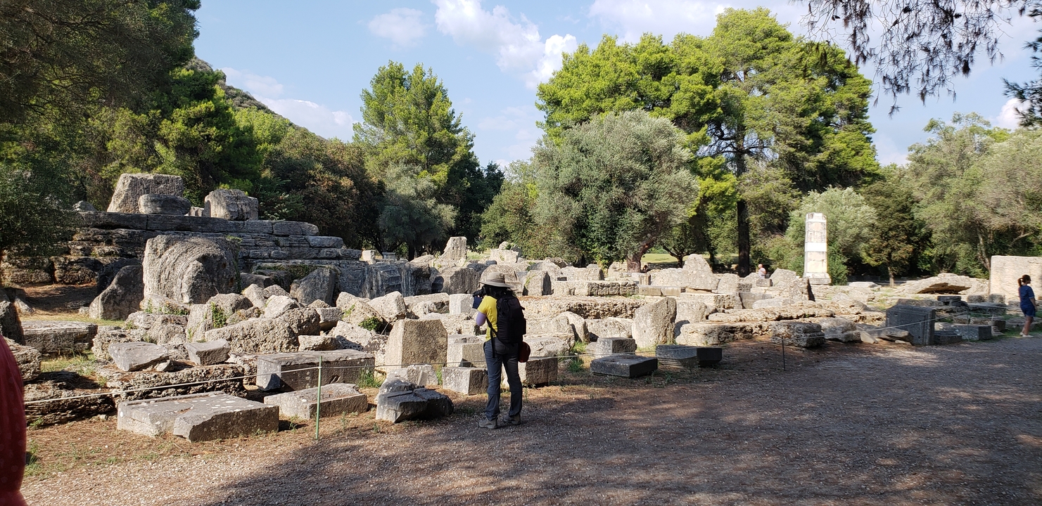 Person exploring ancient ruins surrounded by trees and stones.