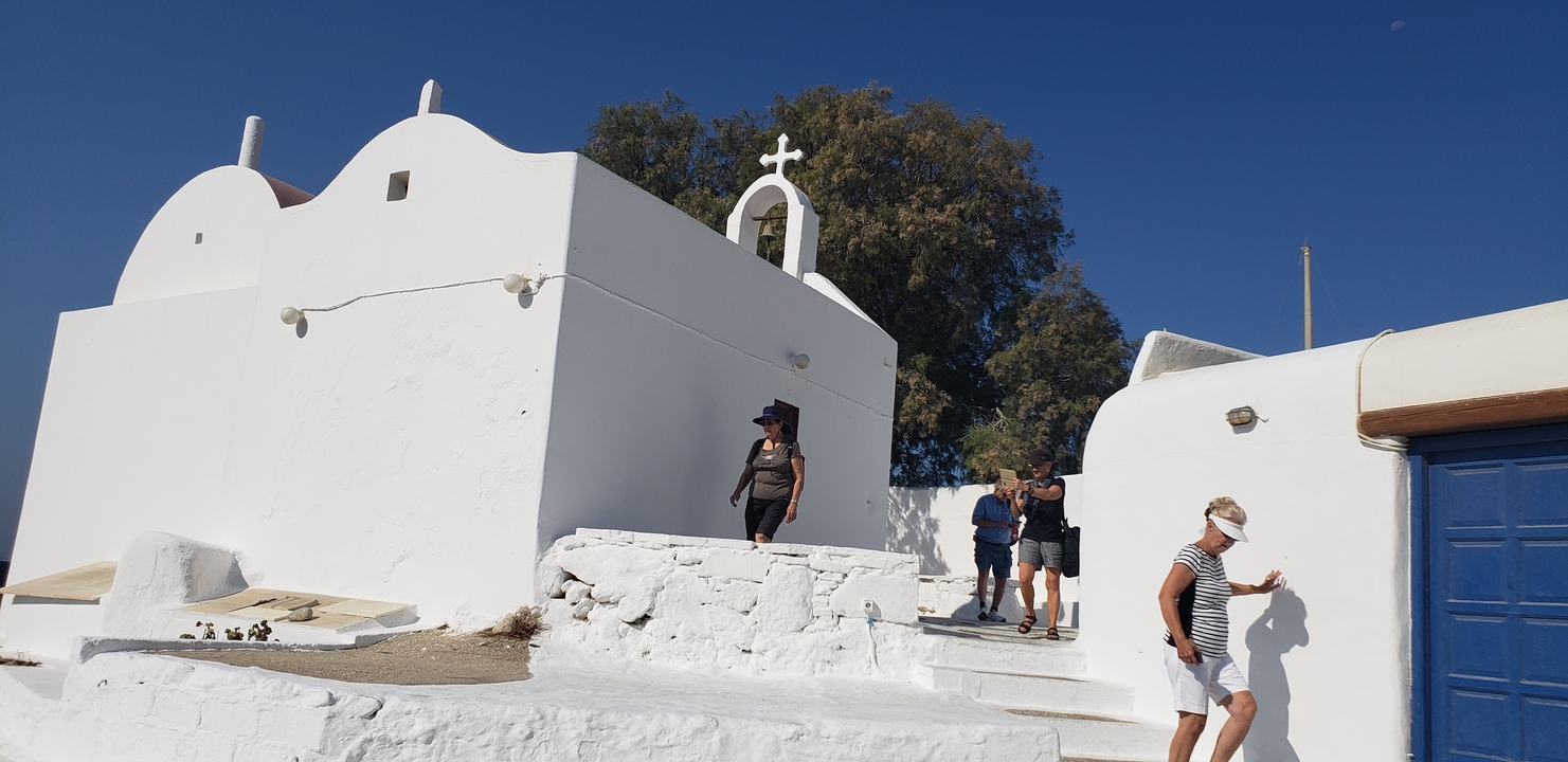 People walking by white buildings with a cross on a clear day.