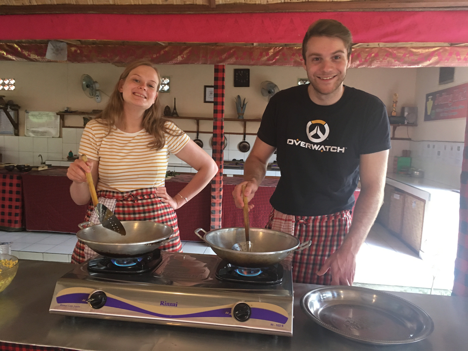Two people cooking with large woks in a traditional kitchen.