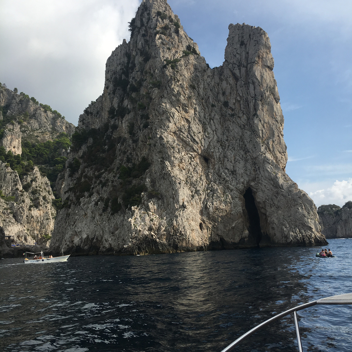 A massive cliff formation in the sea with boats nearby.