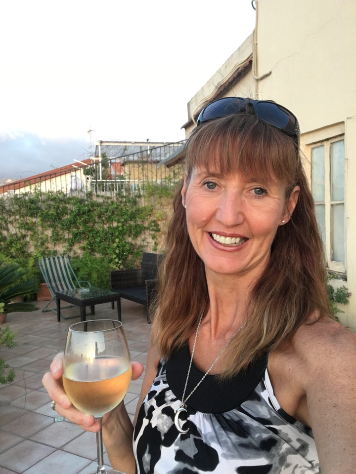 A smiling woman outdoors with a patio and greenery in the background.