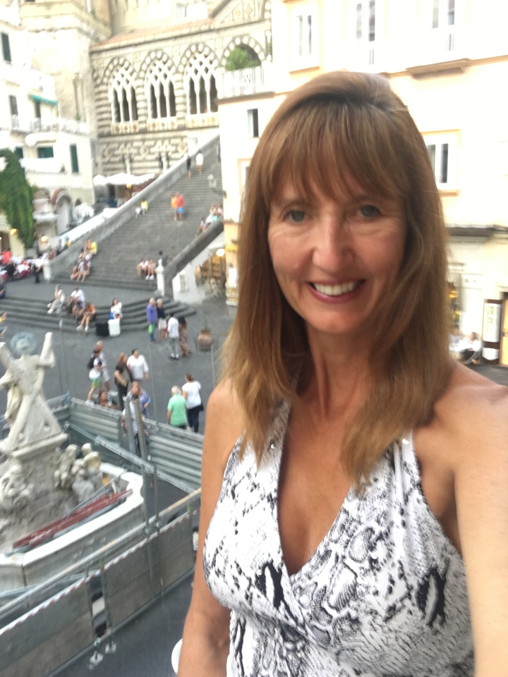 A woman taking a selfie with a blurred cityscape and steps in the background.