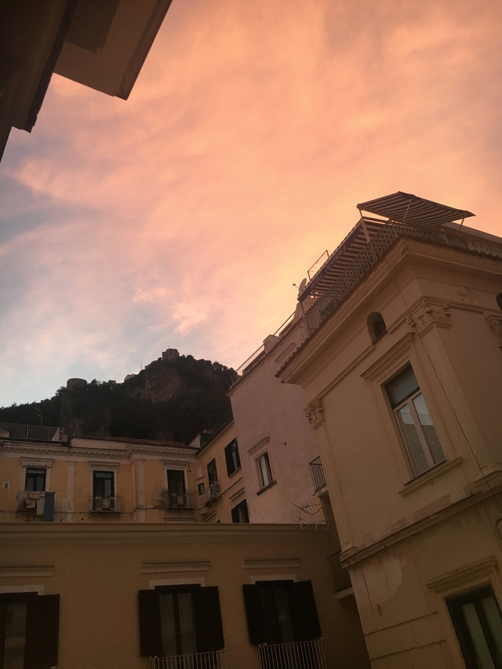 Silhouettes of buildings and a hill against a pink sunset sky.