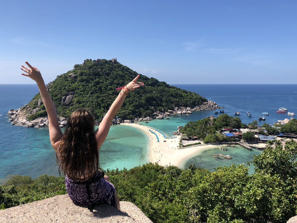 Woman with arms raised looking at a tropical island.