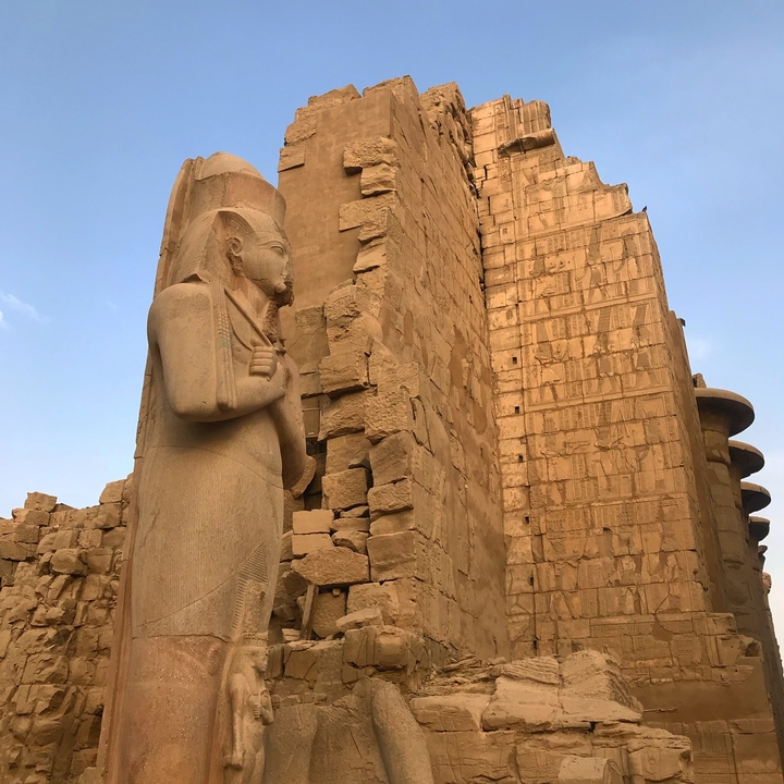 Statue of an Egyptian figure next to ancient ruins.