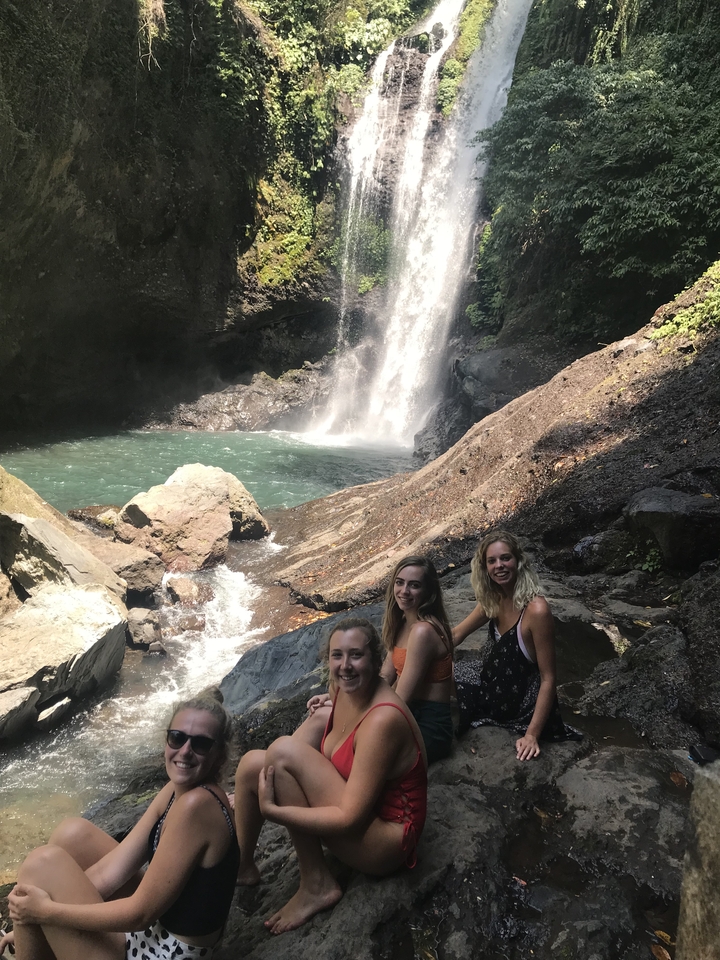 Three people near a waterfall in a lush, tropical setting.