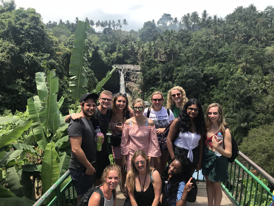 Group of people posing with a lush green jungle and waterfall behind.