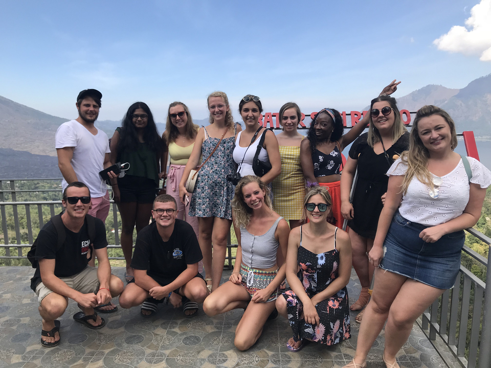 Tour group at a scenic viewing platform with a sign in Bali.