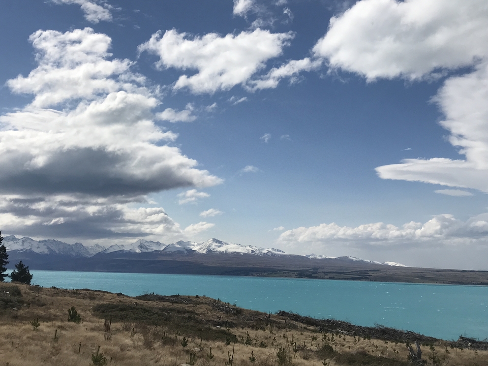 Turquoise lake with distant mountains under cloudy sky.