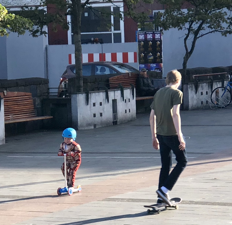 Young boy on a scooter with an adult walking nearby.
