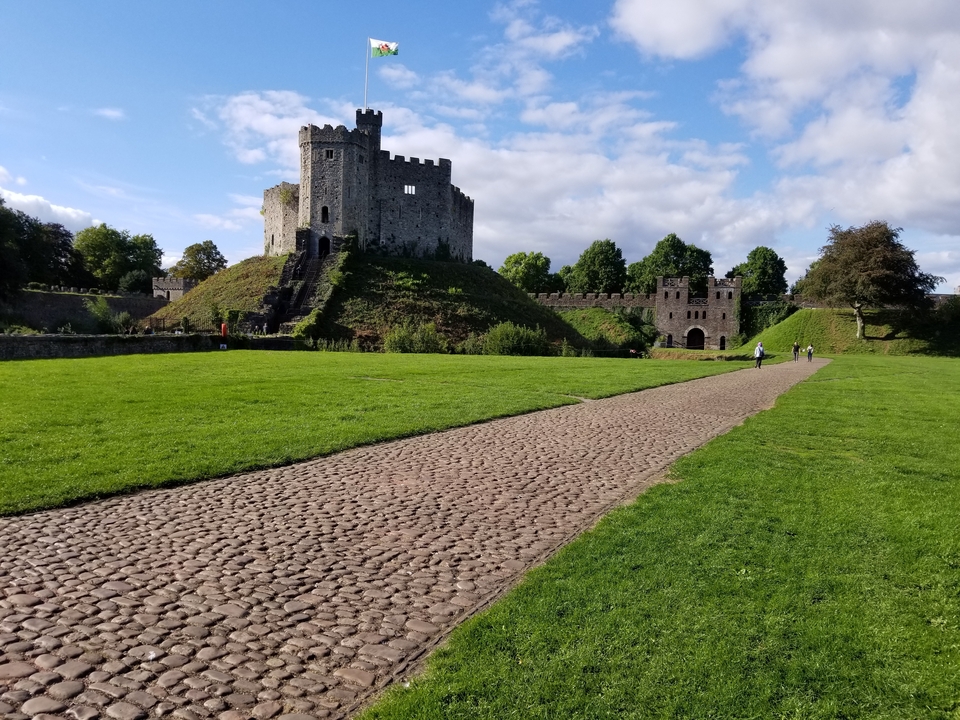 People walking near an ancient castle with lush green field.