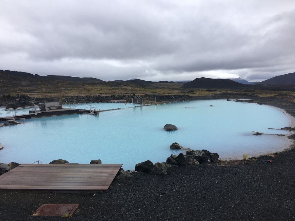 Geothermal pool on a rocky landscape with cloudy sky.