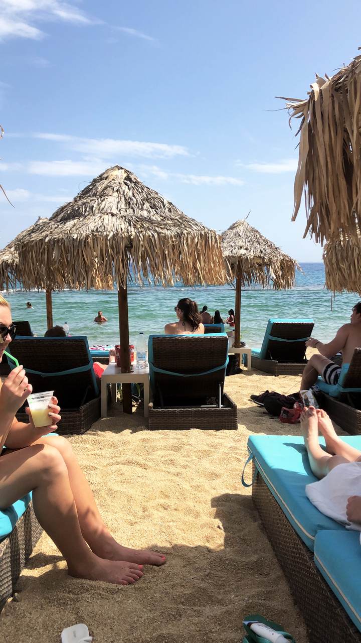 People relaxing on sun loungers under thatched umbrellas by the beach.