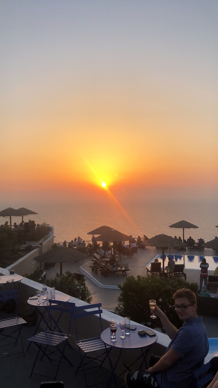 Sunset view over the ocean with silhouettes of people and umbrellas.