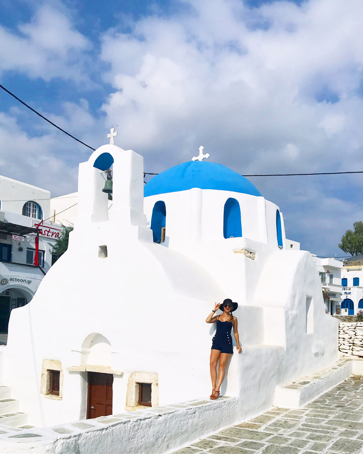 Person posing in front of a traditional white and blue church.