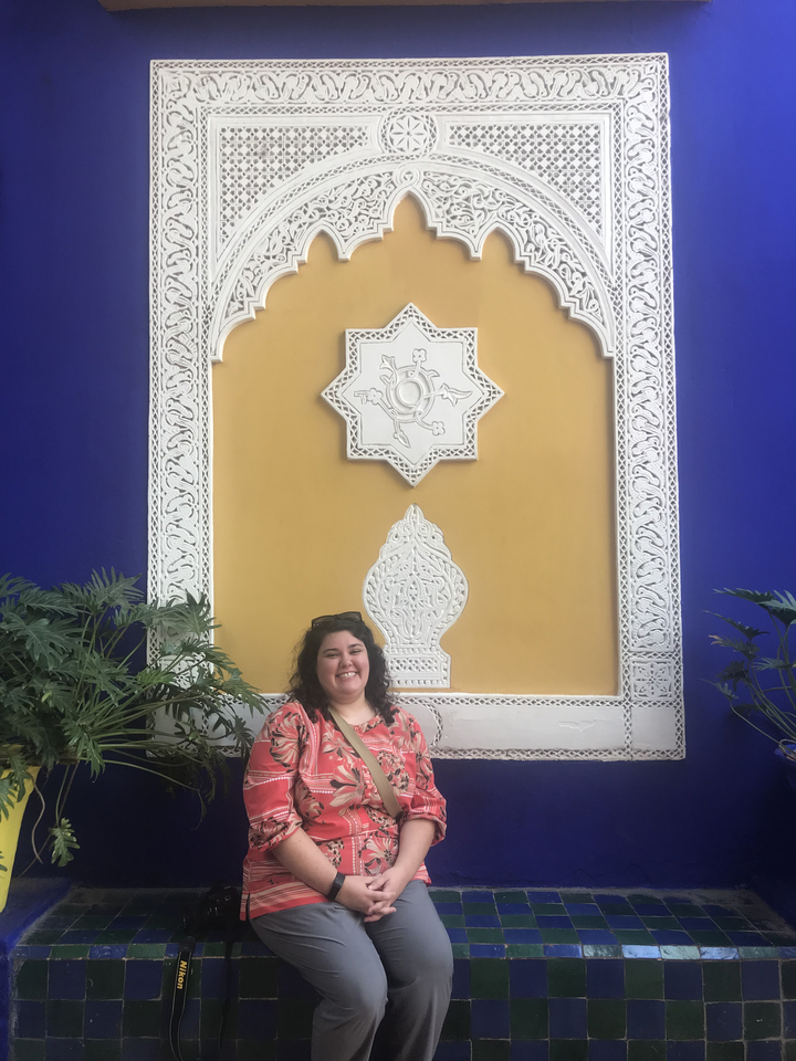 Person posing against decorative wall with plants.