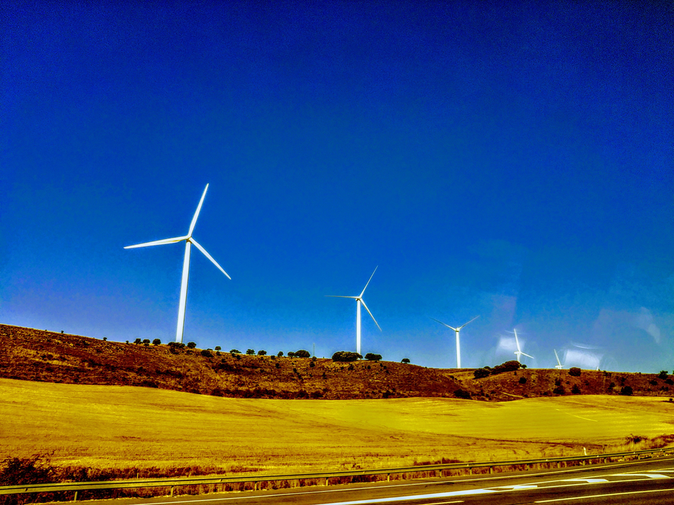 Wind turbines on a hill under a clear blue sky.