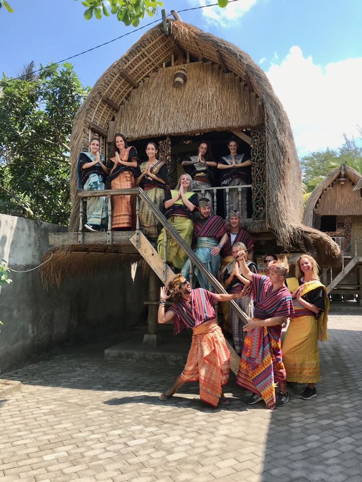 Group of people in traditional dress posing in front of a traditional house.