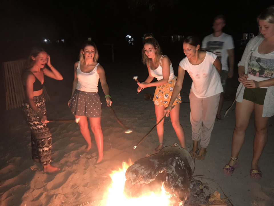 Groupe de personnes autour d'un feu de camp sur la plage en train de faire griller des guimauves.