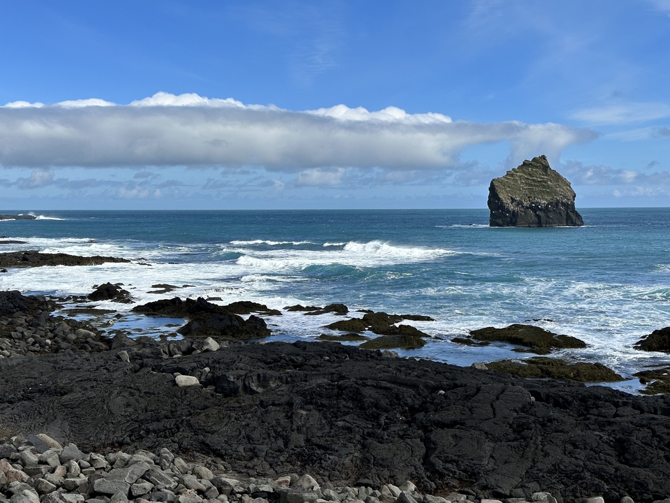 A rocky shoreline with waves crashing and a solitary rock formation.